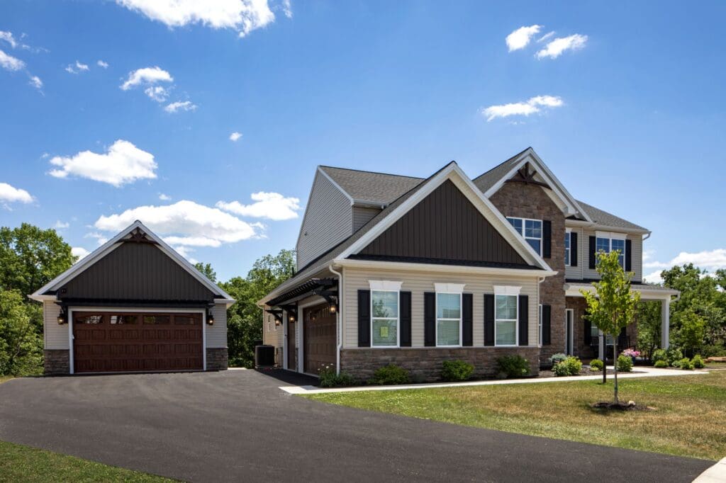 Two-story suburban house with attached and newly built detached garages, dark roof, brown and white exterior, and a paved driveway—perfect inspiration for home remodeling Central PA under a blue sky with scattered clouds.