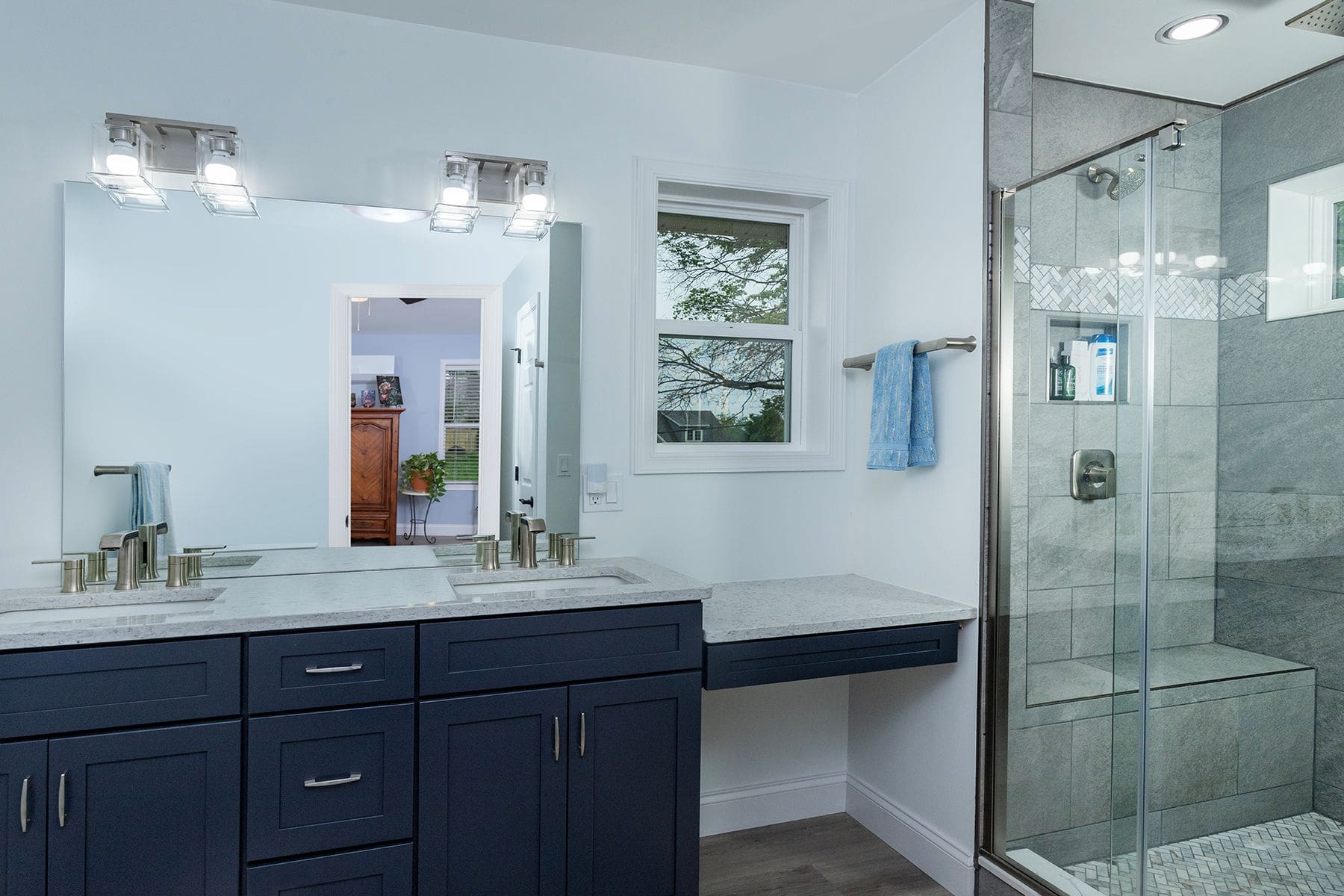 Modern bathroom with a double-sink vanity, blue cabinets, wall mirror, small window, and glass-enclosed shower—perfect inspiration for your next home remodeling Harrisburg project.