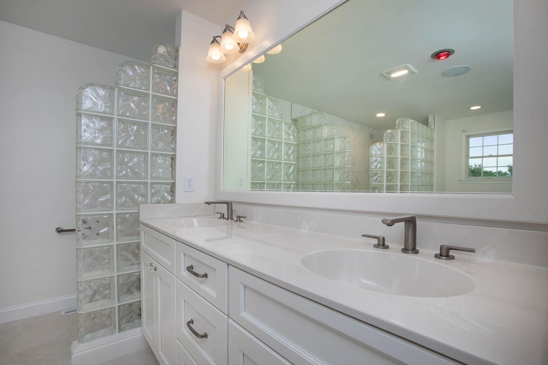 Modern bathroom with double sinks, white cabinets, large mirror, and a walk-in shower enclosed by glass blocks—perfect for Central PA renovations or home remodeling projects.