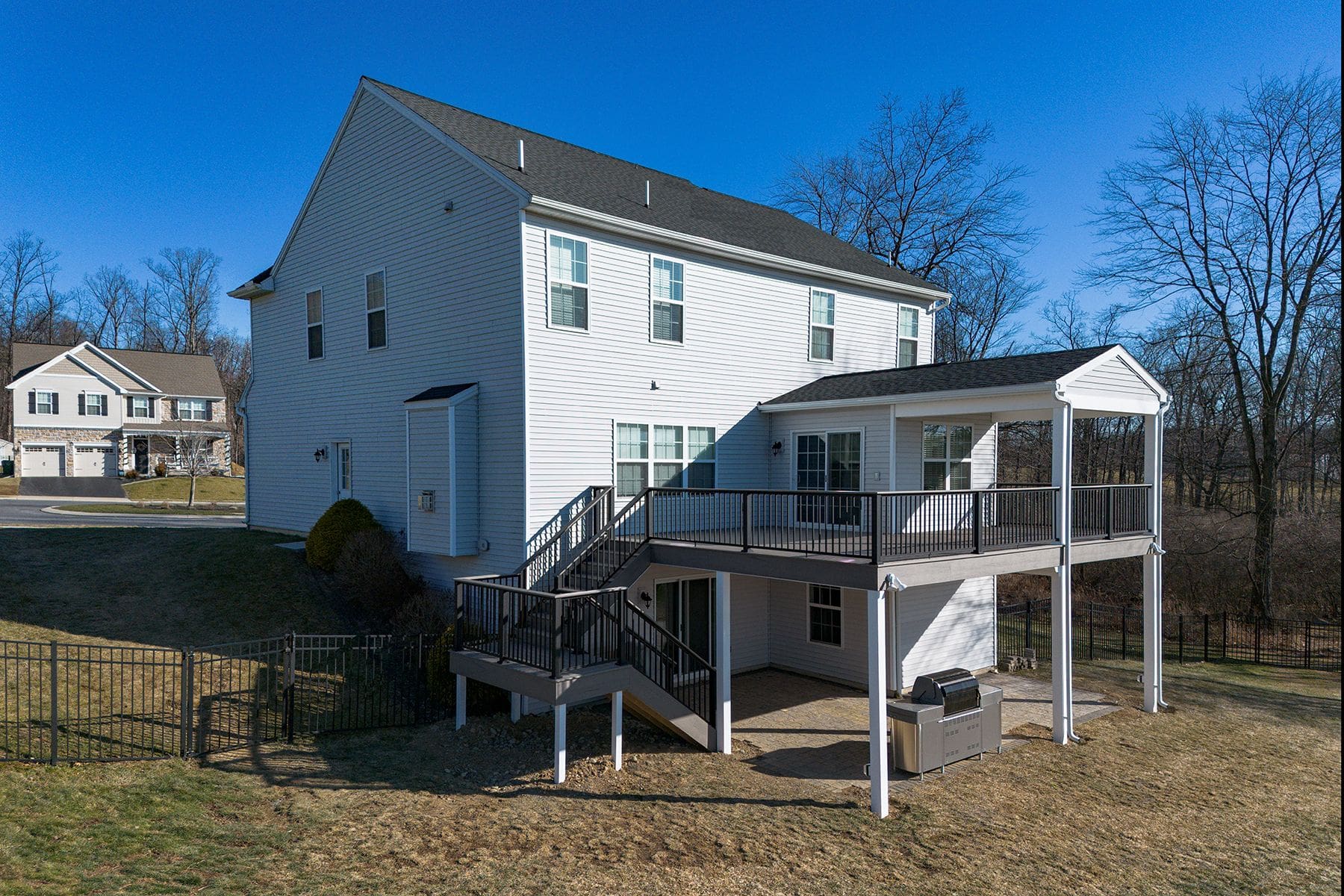 Two-story white house with a covered porch, elevated deck, and stairs leading to a patio area with a grill in the backyard—perfect for your next home remodeling Mechanicsburg project.