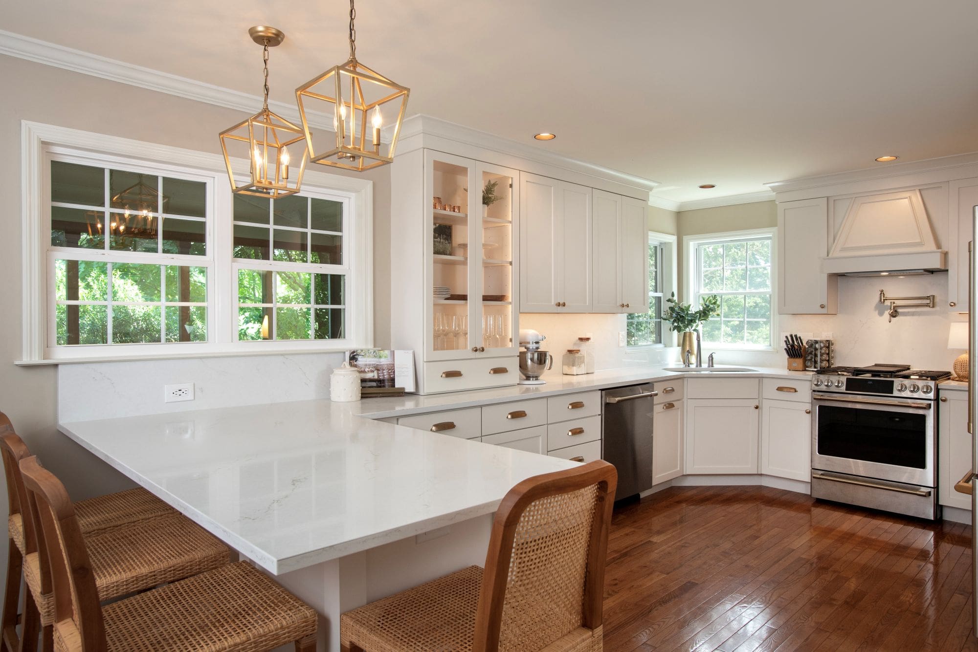 Bright kitchen with white cabinets, marble countertops, stainless steel appliances, wood flooring, a corner sink, and a breakfast bar with four wicker chairs—perfect for your next kitchen remodeling Harrisburg project.